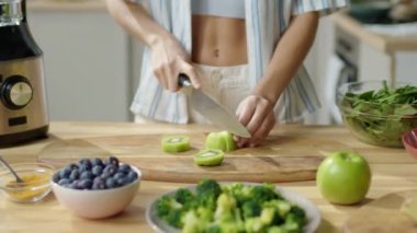 Mutfak masasında taze kivi keserken evde sağlıklı yiyecekler hazırlayan sıska kadının gayri resmi.