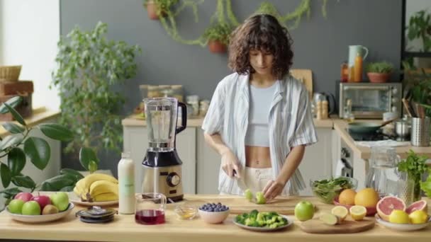 自宅で健康的な食べ物を調理しながらキウイで新鮮なキウイを切った若い女性の中型ショット — ストック動画