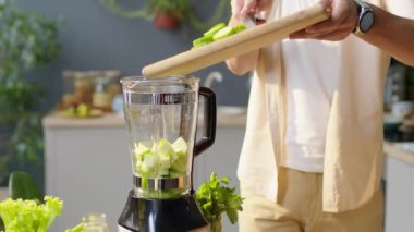 Evde sağlıklı vejetaryen içeceği hazırlarken adamın blender 'a taze salatalık parçaları eklerken çekilen kesikleri yukarı kaldır.