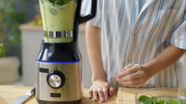 Kırpılmış bir kadının blendırı açarken ve kapağı tutarken evde yeşil smoothie yaparken çekilen pozunu kaldır.