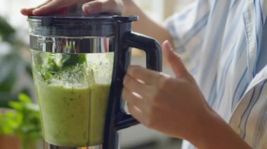 Mutfakta yeşil smoothie yaparken elinde blender tutan bir kadının yakın plan çekimleri.