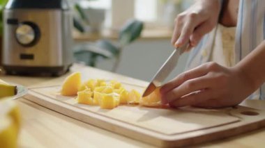 Mutfak masasındaki ahşap tahtada taze portakal kesen kadının yakın plan çekimleri.