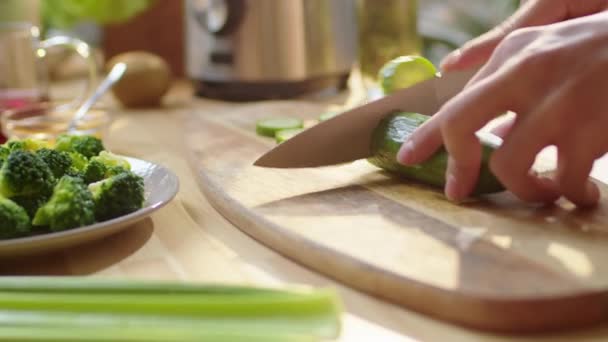 在厨房桌子边的木板上切新鲜黄瓜 同时在家里准备健康饭菜的人的近照 — 图库视频影像