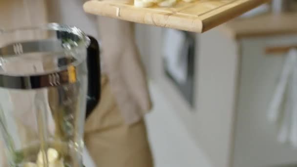 自宅でキッチンでフルーツスムージーを作っている間 バナナスライスをブレンダーに置く男のチルトアップショット — ストック動画