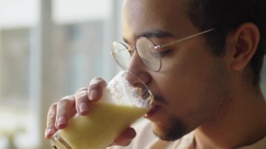Ortadoğulu genç bir adamın cam suyundan taze meyve suyu içerken ve evde gün boyu tadını çıkarırken yakın plan çekimleri.