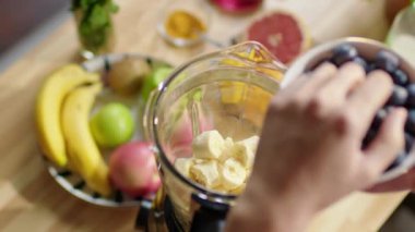 Yüksek açılı, tanınmayan bir kadının ellerini muz balığıyla karıştırıp meyve suyu hazırlarken taze yaban mersini koyarken çek.