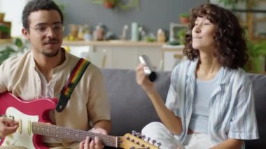 Neşeli Gen Z adamı, kız arkadaşı gibi gitarla müzik çalıyor ve evde birlikte eğleniyor.