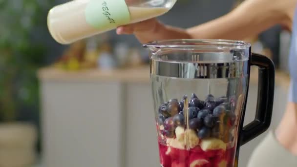 在家里厨房里把纯素牛奶倒入水果和浆果的搅拌机里 同时在厨房里把它做得柔滑的时候 近距离地拍了照 — 图库视频影像