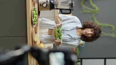 Mutfakta durup taze sebzelerden bahsederken dijital kamerayla sağlıklı yemek blogu çekilen vejetaryen bir kızın dikey çekimi.