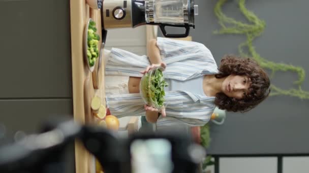 キッチンに立って デジタルカメラで健康的な食品ブログを撮影しながら新鮮な野菜について話すビーガンガールの垂直撮影 — ストック動画