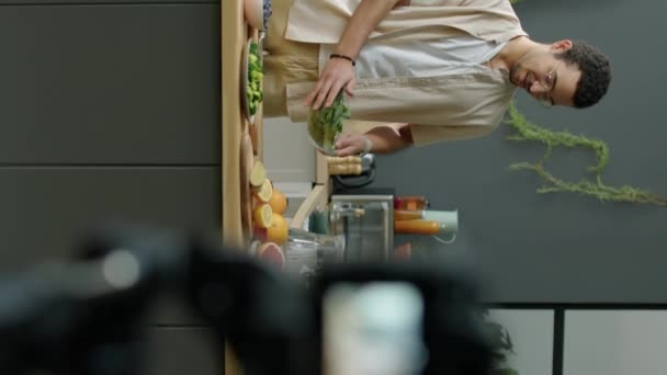 キッチンに立って デジタルカメラで健康的なフードブロッグを撮影しながら滑らかな食材について語るヴィーガン男性の垂直撮影 — ストック動画