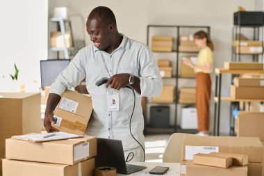 Çevrimiçi dükkanlarda müşteriler tarafından sipariş edilen eşyalarla dolu kutular üzerinde soru cevap kodlarını tarayan mutlu Afrikalı genç bir Amerikalı.