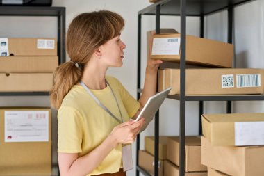 Pazar yerinin genç bayan sahibinin yan görünüşü paketlenmiş kutularda müşteriler hakkındaki kişisel verileri kontrol ederken siparişlerle birlikte beklemede.