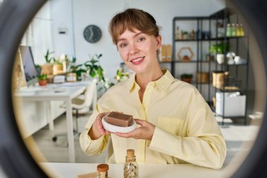 Kameranın önünde oturup el yapımı sabundan bahsederken yeni kişisel bakım ürünleri hakkında canlı yayın yapan mutlu genç bir kadın.