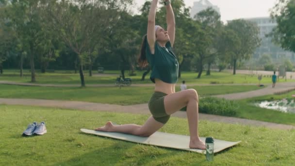 在室外练习文雅瑜伽的同时 让穿着运动服和头带的女人在公园的练习场垫上做相扑 — 图库视频影像