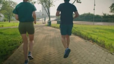 Arka planda spor kıyafetleriyle parkta kaldırımda koşan atletik çiftin sabah birlikte dışarıda egzersiz yaparken çekimleri var.
