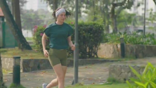 清晨训练时穿着运动服的年轻健康女子在公园人行道上奔跑的慢镜头 — 图库视频影像