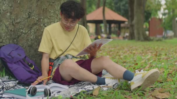 Asiatisk Mandlig Studerende Sidder Tæppe Efter Træ Læser Lærebog Tager – Stock-video