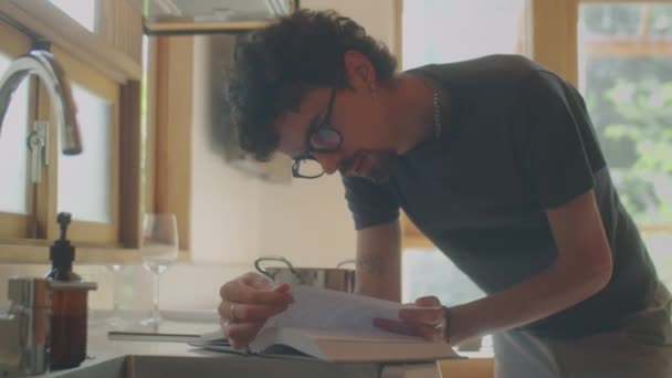 Tiro Médio Homem Óculos Apoiados Balcão Cozinha Livro Leitura Enquanto — Vídeo de Stock