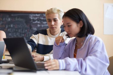 Sınıf arkadaşına sunum yapan kendine güvenen genç Asyalı adama odaklan. Hem onun yanında oturuyor hem de dizüstü bilgisayarına bakıyor.