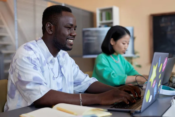 在信息学课上用笔记本电脑键盘打字的非洲裔美国人微笑 同时致力于开发新的解码数据软件 — 图库照片