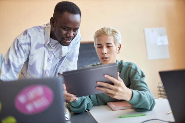 在讨论新软件或准备项目时 带着平板电脑在屏幕上解释同学数据的自信的亚洲男生 — 图库照片
