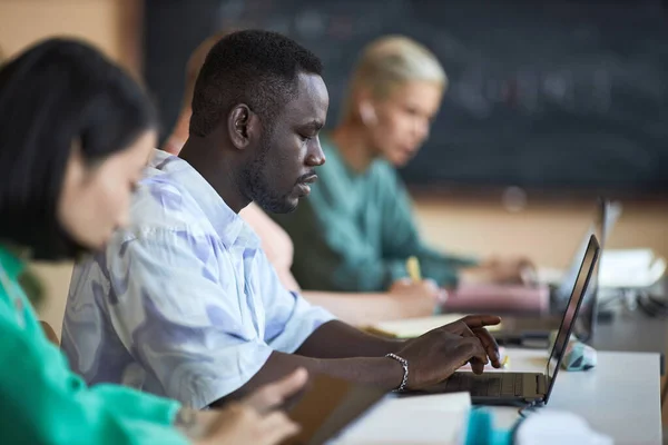 非洲裔美国高中生坐在多元文化同学中间和解码数据时使用笔记本电脑的侧视图 — 图库照片