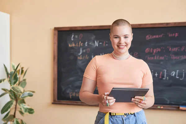 快乐的年轻女教师或高中女生穿着粉色T恤 靠着黑板站在那里 看着相机时 用平板电脑 — 图库照片