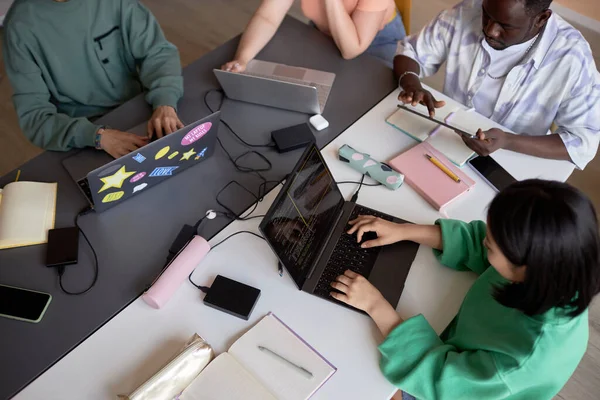 一组年轻学生坐在桌旁 使用移动设备 其中一人在笔记本电脑键盘上打字 并对数据进行解码 — 图库照片