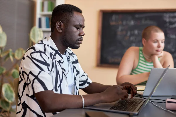 从侧面看认真的非裔美国人看笔记本电脑键盘 并思考新学校信息学项目的要点 — 图库照片