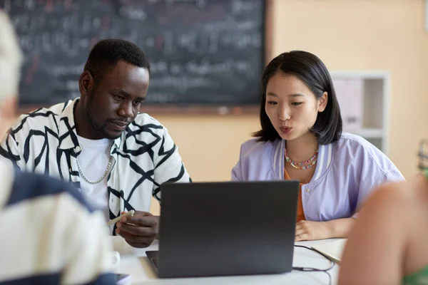 年轻自信的亚洲学生和她的非洲裔美国同学在讨论演示或项目要点时看着笔记本电脑屏幕 — 图库照片
