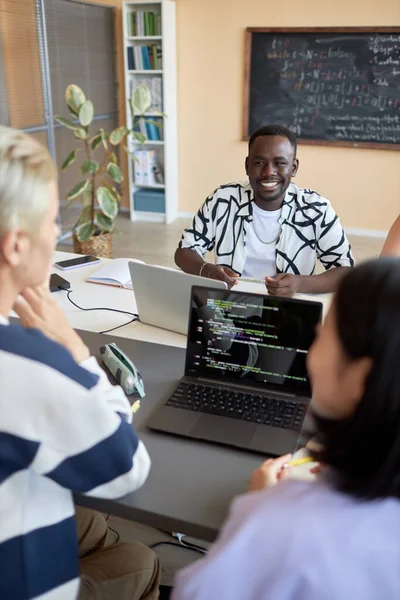 年轻快乐的非裔美国人 与坐在他面前的两个同学进行了讨论 并在笔记本电脑屏幕上解码数据 — 图库照片