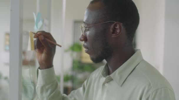 Średnie Zbliżenie Zdjęcia Afroamerykańskiego Biznesmena Piszącego Lepkiej Nucie Przymocowanej Szklanej — Wideo stockowe
