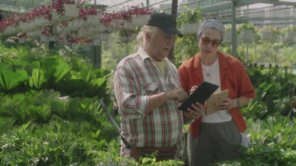 Senior Kweker Bespreekt Iets Tablet Met Vrouwelijke Collega Terwijl Aantekeningen — Stockvideo