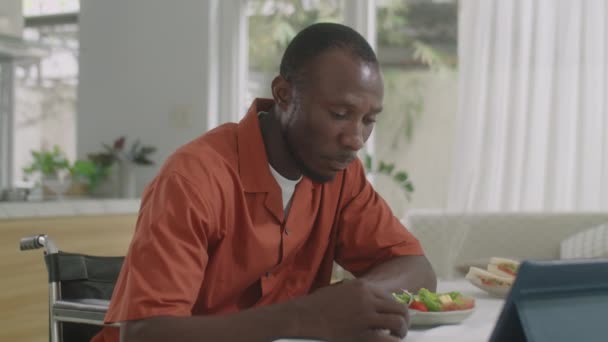 坐在轮椅上的非裔美国人白天在家里吃饭 在数字平板电脑上看东西 — 图库视频影像