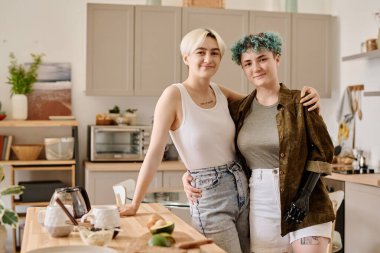 Mutfakta yemek hazırlarken kameraya sarılıp bakan genç lezbiyen çiftin portresi.
