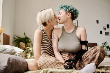 Sevecen lezbiyen çift yatakta oturuyor ve öpüşüyor.