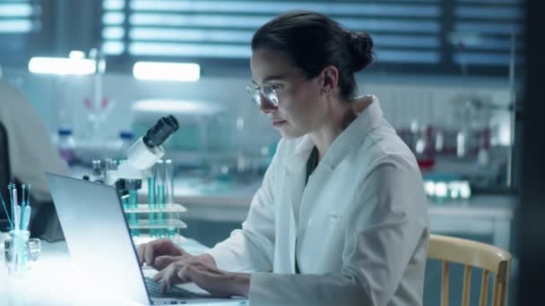 在科学实验室的办公桌前工作时 在笔记本电脑上用实验室外套打字的女化学家中的照片 — 图库视频影像
