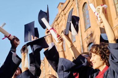 Bir grup mutlu öğrenci diplomalarıyla ellerini kaldırarak üniversiteyi bitiriyor.
