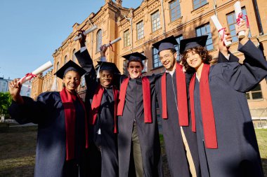 Bir grup mutlu öğrenci üniversitenin yanında diplomalarıyla ayakta duruyor.