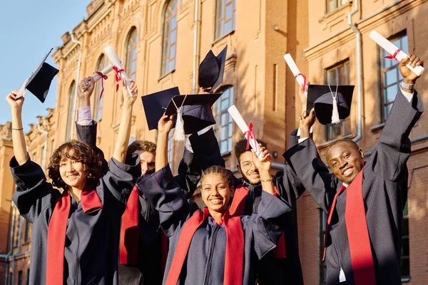 持文凭站在室外举手的多族裔学生群体 — 图库照片