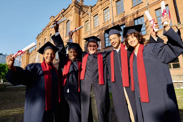 大学の近くで卒業証書を持って立っているゴウンの幸せな学生のグループ — ストック写真