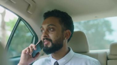Resmi gömlekli ve kravatlı bir iş adamı taksideyken cep telefonuyla konuşuyor.