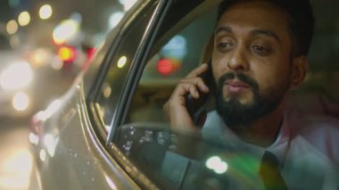 Arka koltukta oturan, açık pencereden bakan ve gece sürerken cep telefonuyla konuşan iş adamının arabasının dışından görüntüsü
