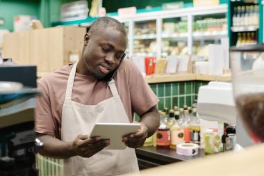 Cep telefonuyla konuşurken tablet bilgisayarında online sipariş yazan Afro-Amerikalı bir genç.