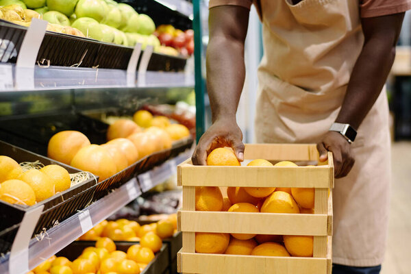 Store employee in uniform laying out fruits on shelves from box