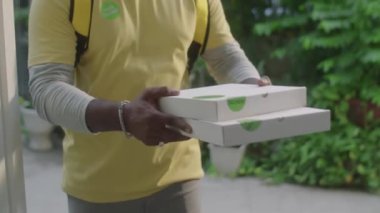 Tanıdık bir teslimatçının eve yemek getirirken iki pizza kutusunu kadın müşteriye vermesi.