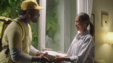 Asyalı kadın kapıyı açıyor, pizzacıdan pizza kutularını alıyor, gülümsüyor ve ona veda ediyor.