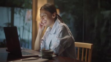 Gülümseyen Asyalı kadın, akşam yemeğini evde geçirirken bilgisayarında video üzerinden el sallıyor ve konuşuyor.