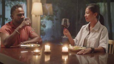 Çeşitli aile çiftleri kadeh tokuşturuyor, kırmızı şarap içiyor ve evde romantik bir akşam yemeği yiyorlar.